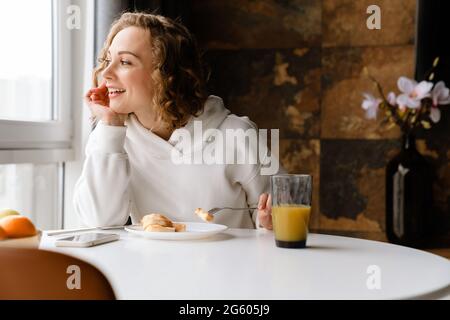 Weiße blonde Frau beim Frühstück, während sie zu Hause am Tisch sitzt Stockfoto