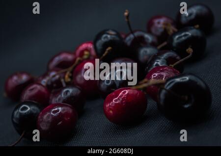 Kirschen mit Wassertropfen auf einem schwarzen Tisch. Reife Kirschen. Süße rote Kirsche. Draufsicht. Rustikaler Stil. Obsttapete Stockfoto