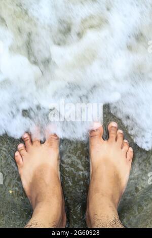 Urlaub am Meeresstrand, Füße auf dem Meer Sand. Am Strand stehend, mit Meereswellen bedecken das Bein, von oben blickend. Stockfoto