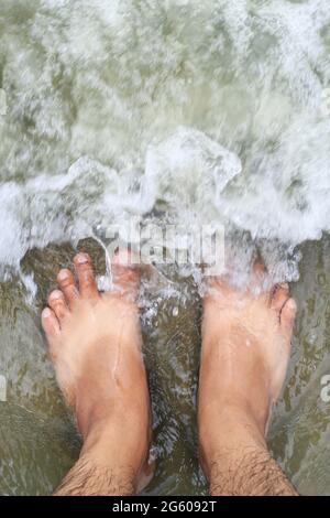 Urlaub am Meeresstrand, Füße auf dem Meer Sand. Am Strand stehend, mit Meereswellen bedecken das Bein, von oben blickend. Stockfoto