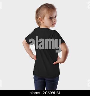 Schwarzes Kinder-T-Shirt auf einem posierten Mädchen in blauen Jeans, auf einem Hintergrund im Studio. Vorlage Baby Kleidung auf Kind, Rücken-und Seitenansicht, fas Stockfoto