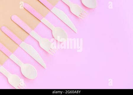 Bambus-Einweglöffel, -Gabeln und -Messer auf beigefarbenem und rosafarbenem Hintergrund. Zero Waste Konzept. Draufsicht, Kopierbereich.