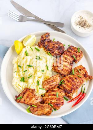 Gegrillte Hühnerschenkel mit Kartoffelpüree, garniert mit Schnittlauch und Zitrone Top Down Food Photography Stockfoto