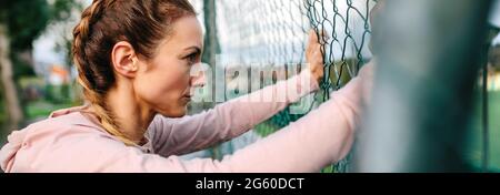 Seriöse Portwoman mit Boxergeflechten, die an einem Metallzaun gelehnt sind Stockfoto