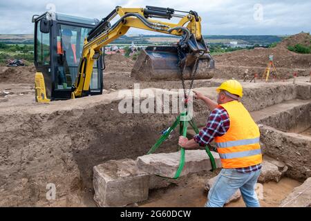 Eisleben, Deutschland. Juli 2021. Die Grabarbeiter heben die Abdeckung eines Sarkophags auf dem Gelände des ehemaligen königlichen Palastes von Helfta ab. Archäologen des Landesamtes für Denkmalpflege und Archäologie Sachsen-Anhalt hatten bereits vor Wochen damit begonnen, die Grundmauern der Kirche Kaiser Ottos des Großen (912-973) aufzudecken. Dabei stießen die Archäologen auf eine große Anzahl von Bestattungen, darunter mehrere Steinkrypten aus dem 10. Bis 15. Jahrhundert. Quelle: dpa picture Alliance/Alamy Live News Stockfoto