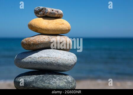 Steinhaufen, der vom kleinsten zum größten übereinander gelegt wird, mit verschiedenen Formen und verschiedenen Farben, mit dem Mittelmeer in der Stockfoto