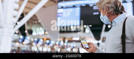 Mann mit digitalem Impfpass am Flughafen am Telefon. Passagier trägt Gesichtsmaske mit digitalem Zertifikat der covid-19-Impfung auf dem Telefon-Display. Stockfoto
