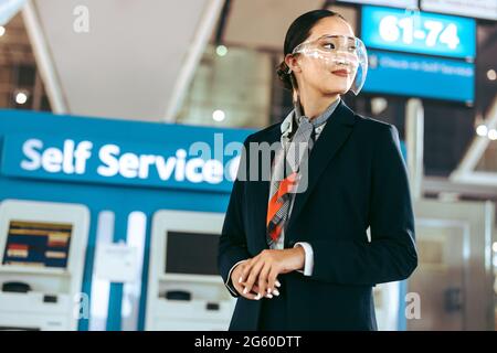 Weibliche Flughafenangestellte in Uniform und Gesichtsschutz schaut weg. Bodenpersonal am Flughafen, das während einer Pandemie arbeitet. Stockfoto