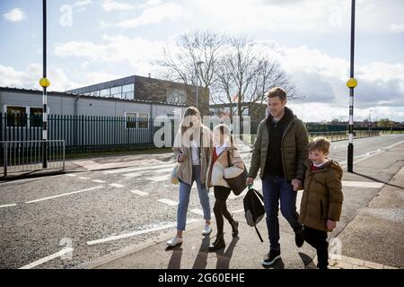 Eine Aufnahme einer vierköpfigen Familie, die sicher den Bürgersteig entlang geht, bringen die Eltern ihre Kinder von der Schule nach Hause. Stockfoto