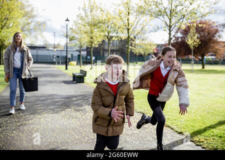 Eine Frontansicht einer kaukasischen Mutter, die mit ihrem Sohn und ihrer Tochter von der Schule nach Hause geht, läuft aufgeregt davon. Stockfoto