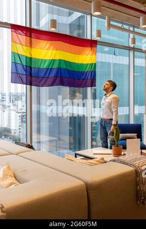 Ein hübscher Mann in legerem Kleid, der die Flagge der LGBT-Gemeinschaft in Erwägung zieht Stockfoto