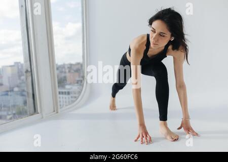 Junge armenische Frau in schwarzer Sportkleidung, die Yoga in Ausfallhaltung praktiziert Stockfoto