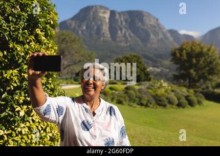 Ältere afroamerikanische Frau, die Selfies mit dem Smartphone im sonnigen Garten macht Stockfoto