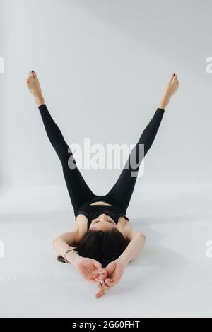 Barfuß armenische Frau in schwarzen Leggings praktiziert Yoga in Verjüngungshaltung auf Weiß Stockfoto