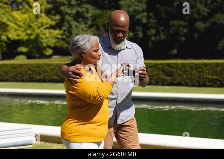 Ältere afroamerikanische Paare verbringen Zeit in sonnigen Garten zusammen mit Smartphone und lächeln Stockfoto