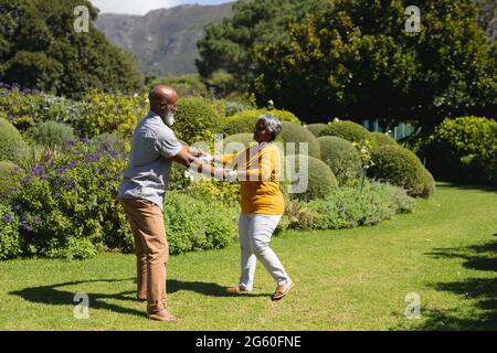 afroamerikanisches Senioren-Paar, das gemeinsam im sonnigen Garten tanzt Stockfoto