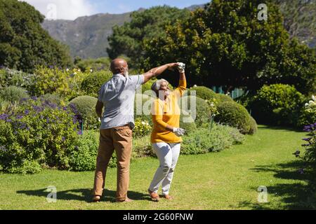 afroamerikanisches Senioren-Paar, das gemeinsam im sonnigen Garten tanzt Stockfoto