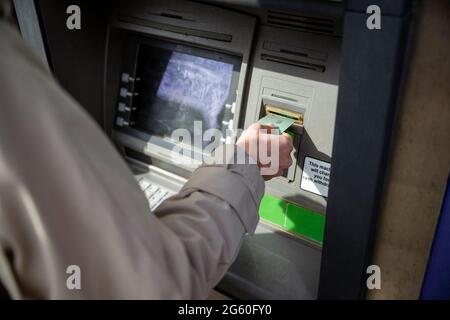 Eine Nahaufnahme einer unkenntlichen kaukasischen Frau, die an einem Geldautomaten auf einer Stadtstraße eine Debitkarte verwendet, in einem legeren Tuch Stockfoto