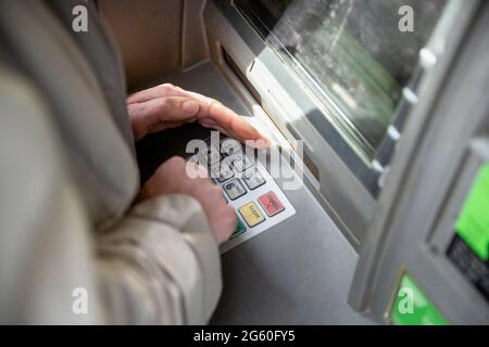 Eine Nahaufnahme einer unkenntlichen kaukasischen Frau, die an einem Geldautomaten auf einer Stadtstraße eine Debitkarte verwendet, in einem legeren Tuch Stockfoto