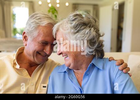 Ältere kaukasische Paare, die auf dem Sofa sitzen und umarmen und lächeln Stockfoto