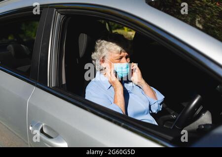 Ältere kaukasische Frau mit Gesichtsmaske im Auto sitzend Stockfoto