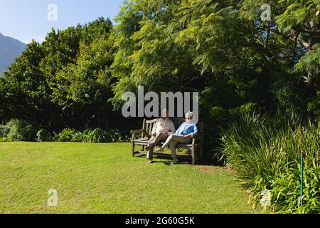 Ein älteres kaukasisches Paar sitzt auf einer Bank zusammen im sonnigen Garten Stockfoto