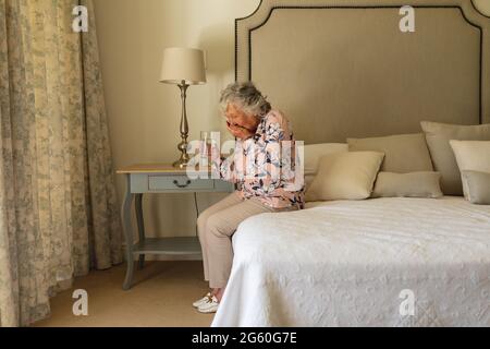 Ältere kaukasische Frau, die auf dem Bett sitzt und Pillen nimmt Stockfoto