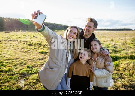 Eine Frontansicht einer kaukasischen Mutter und eines Vaters mit ihrem Sohn und ihrer Tochter, die alle eine Pause vom Gehen machen, indem sie für ein Selfie mit einem lächeln Stockfoto