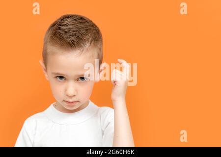 Porträt eines unzufriedenen kleinen Jungen, der sich mit einem Finger auf den Kopf klopft, wild und grausam aussieht, unzufriedene Stirnrunzeln Stockfoto