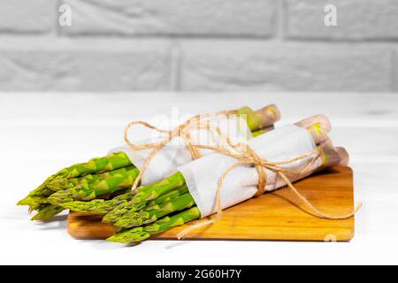 Frischer grüner Spargel auf Holztisch auf weißem Hintergrund. Gesunde pflanzliche Ernährung. Vegetarismus. Gemüsetapete. Stockfoto
