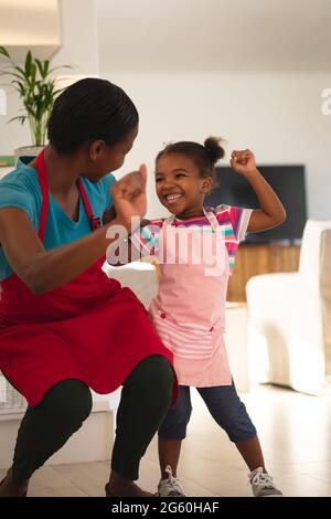 Glückliche afroamerikanische Mutter und Tochter, die in der Küche gebackt haben und dabei mit Schürzen feiern Stockfoto