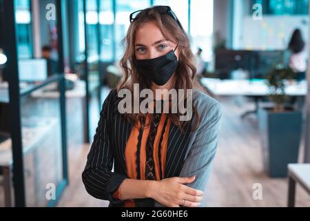 Porträt einer kaukasischen Geschäftsfrau mit Gesichtsmaske und Kollegen im Hintergrund Stockfoto