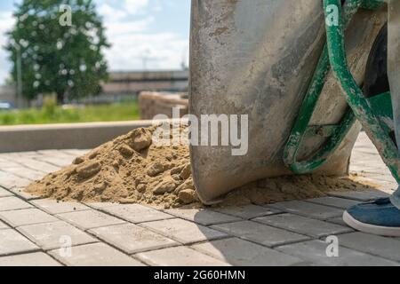 Nahaufnahme eines Mannes aus einer Schubkarre, der Sand auf einen neuen Bürgersteig gießt, um die Risse zu versiegeln Stockfoto