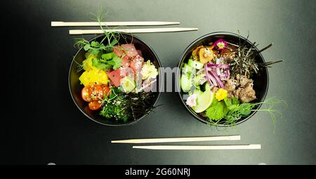 Salate mit Thunfisch und Rindfleisch in Schüsseln auf den Tisch stecken. Zwei Schüsseln Poke-Salat mit Essstäbchen auf grauem Hintergrund. Asiatischer Salat mit Meeresfrüchten Stockfoto