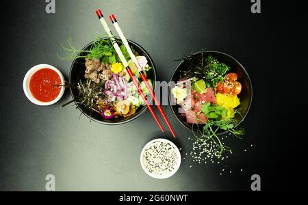 Salate mit Thunfisch und Rindfleisch in Schüsseln auf den Tisch stecken. Zwei Schüsseln Poke-Salat mit Essstäbchen auf grauem Hintergrund. Asiatischer Salat mit Meeresfrüchten Stockfoto