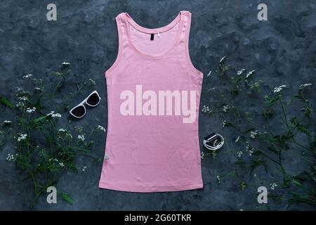 Tanktop aus rosa Baumwolle auf dunklem Hintergrund. Leere einfarbige T-Shirt-Vorlage für kreatives Design. Weibliche Sommer Sonnenbrillen Kleidung Mode ärmellos Stockfoto