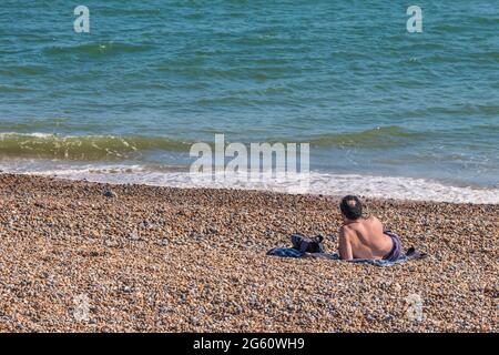 Ein Mann, der an einem heißen Tag in Hastings, Großbritannien, am Strand saß Stockfoto