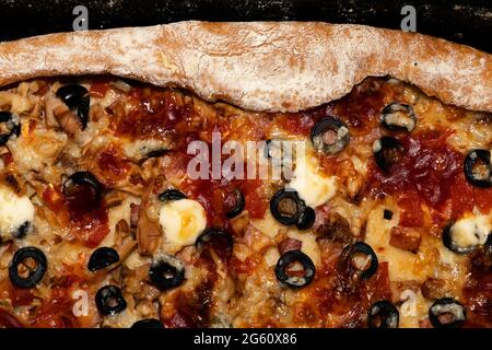 Fleischpizza mit Käse, Oliven und Tomaten, gewürzt mit Sauce und einer Teigkante darauf Stockfoto