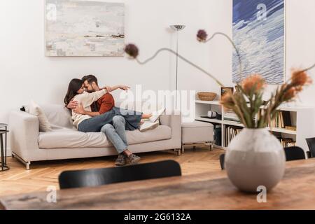 Seitenansicht des Mannes, der lächelnde Freundin auf der Couch im Wohnzimmer umarmt Stockfoto