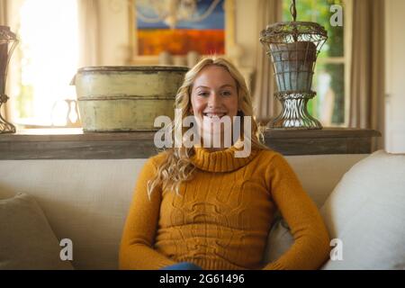 Porträt einer glücklichen kaukasischen Frau, die im luxuriösen Wohnzimmer auf der Couch sitzt und lächelt Stockfoto