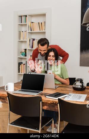 Fröhliches Paar mit Videoanruf auf dem Laptop in der Nähe von Kaffee und Zeitung Stockfoto
