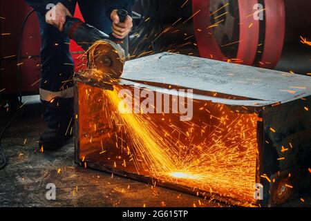 Ein Arbeiter schneidet Metall mit einem Handschleifer in der Produktionshalle und es fliegen leuchtende Funken. Eine echte Arbeitsumgebung. Ein Mann bei der Arbeit. Stockfoto