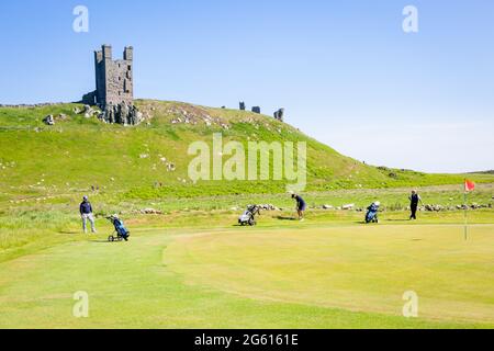 Menschen, die mit Dunstanburgh Castle in der Ferne Golf spielen, Northumberland, Großbritannien Stockfoto