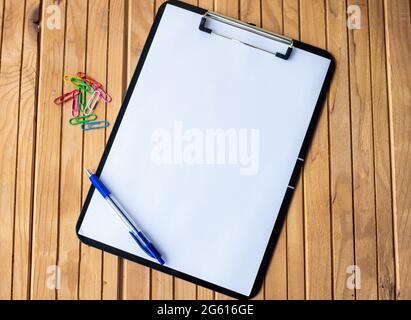 Plain Office Clipboard mit einem Stapel von Stifte in EINEM Halter auf einem Tisch. Leeres Papierblatt mit bunten Bleistiften Behälter auf EINEM Schreibtisch platziert. Stockfoto