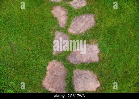 Landschaftsgestaltung des Gartenpfades aus natürlichem grobem Stein, entlang der man zum Hinterhof gehen und zum Haus auf Sommer grünen Rasen Draufsicht Textur mit s gehen Stockfoto