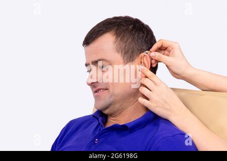 Otolaryngologe, der Hörgeräte in das Ohr des Patienten legt, während der Patient im Klinikschrank sitzt. Stockfoto