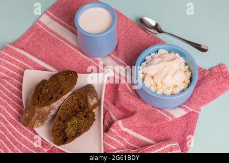 Quark in einer blauen Schüssel mit Sauerrahm und Honig. Geröstetes Brot auf einem Teller. Frühstück am Morgen. Stockfoto