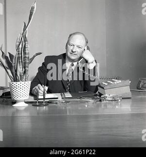 1970s, ein historischer Geschäftsleiter, der mit einem Pad und einem Stift am Telefon am Schreibtisch sitzt, England, Großbritannien, mit einer Hausanlage und einem Glasaschenbecher auf dem Schreibtisch. Stockfoto