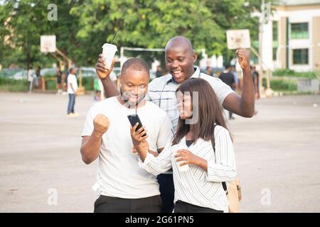 Drei junge afrikanische Menschen schauen im Freien in ihr Telefon Stockfoto
