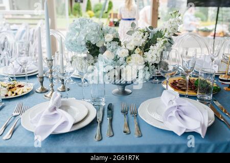 Schöne Tischkulisse für eine Veranstaltung auf einer Terrasse. Leere Teller mit Servietten und ein paar Vorspeisen dazwischen. Niedriger Winkel. Stockfoto